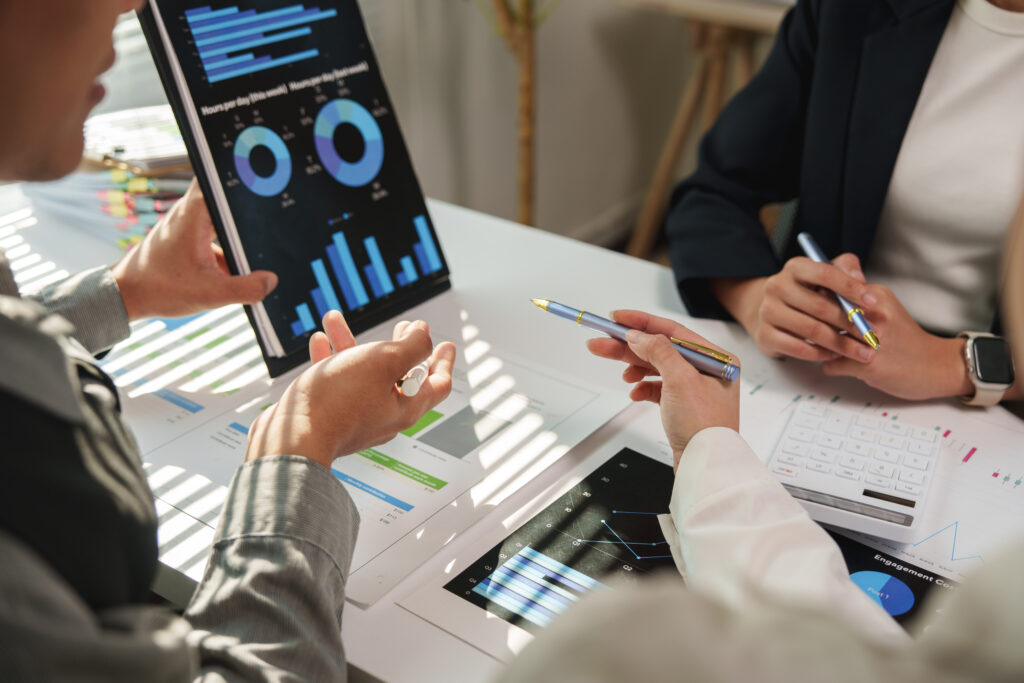 Business team analyzing financial charts and statistics displayed on digital tablet and printed documents, discussing company performance and planning strategies during meeting